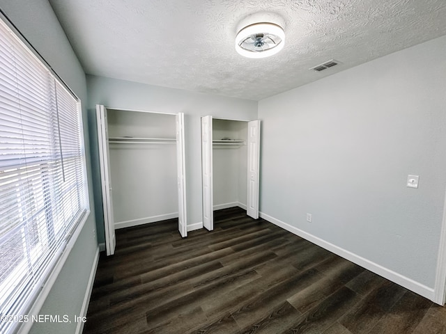 unfurnished bedroom featuring a textured ceiling, dark hardwood / wood-style floors, and multiple closets