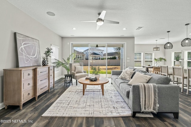 living room featuring ceiling fan, a wealth of natural light, dark wood-type flooring, and a textured ceiling