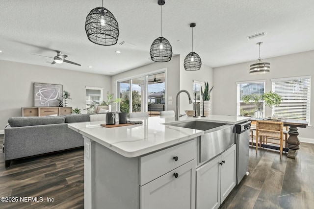 kitchen featuring dark wood-type flooring, stainless steel dishwasher, decorative light fixtures, and a kitchen island with sink