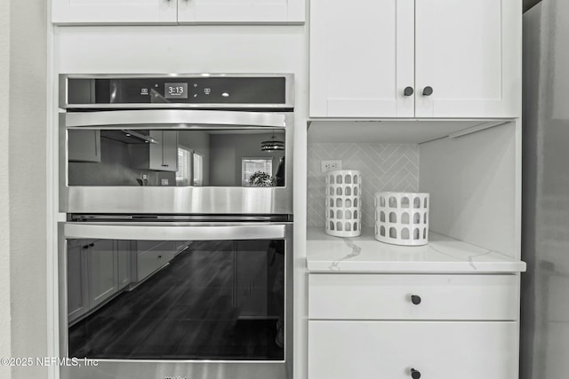 kitchen with white cabinetry, light stone countertops, double oven, and backsplash