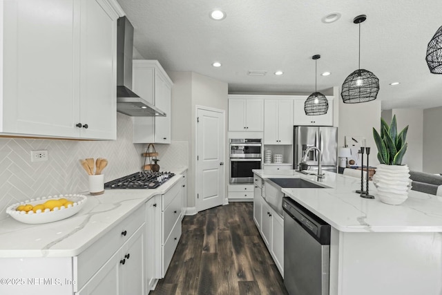 kitchen with white cabinetry, decorative light fixtures, appliances with stainless steel finishes, a kitchen island with sink, and wall chimney range hood