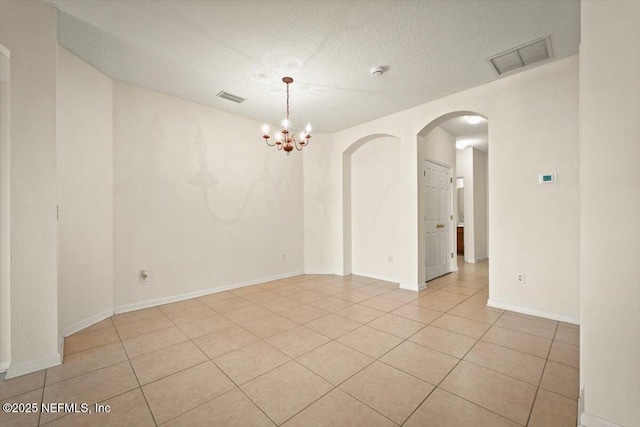 tiled spare room featuring a textured ceiling and an inviting chandelier