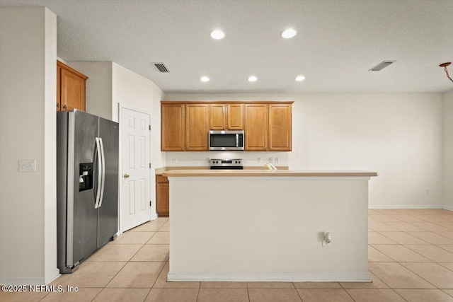 kitchen with light tile patterned floors, an island with sink, a textured ceiling, and appliances with stainless steel finishes