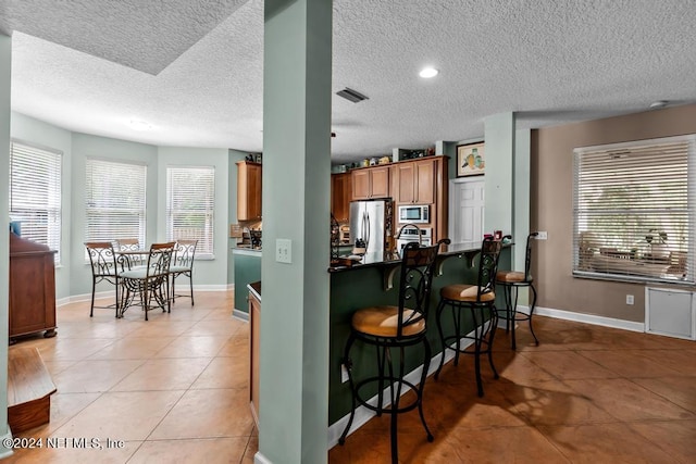 kitchen featuring a breakfast bar, brown cabinets, light tile patterned floors, stainless steel appliances, and visible vents