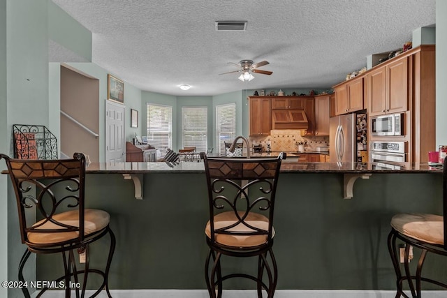 kitchen with a breakfast bar area, stainless steel appliances, premium range hood, visible vents, and decorative backsplash