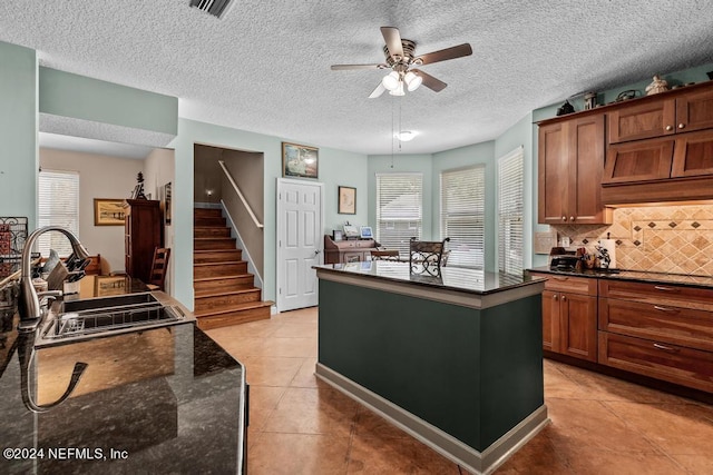 kitchen with light tile patterned floors, tasteful backsplash, a ceiling fan, a kitchen island, and a sink