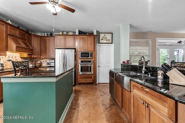 kitchen with backsplash, appliances with stainless steel finishes, a ceiling fan, a sink, and dark stone counters