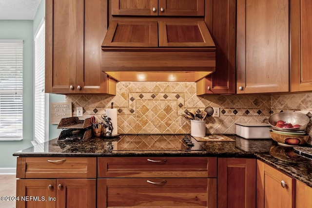 kitchen with black electric stovetop, tasteful backsplash, a wealth of natural light, dark stone countertops, and premium range hood