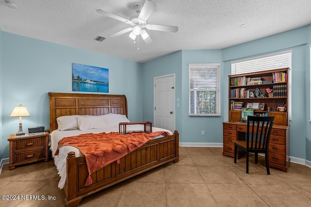 bedroom with a textured ceiling, ceiling fan, light tile patterned floors, visible vents, and baseboards