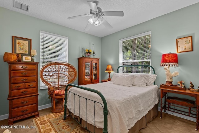 tiled bedroom with baseboards, visible vents, ceiling fan, and a textured ceiling