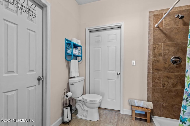 bathroom with baseboards, tiled shower, toilet, and wood finished floors