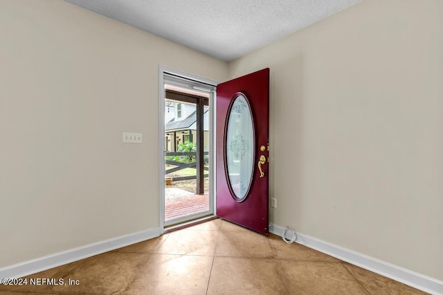 entrance foyer with a textured ceiling, light tile patterned floors, and baseboards