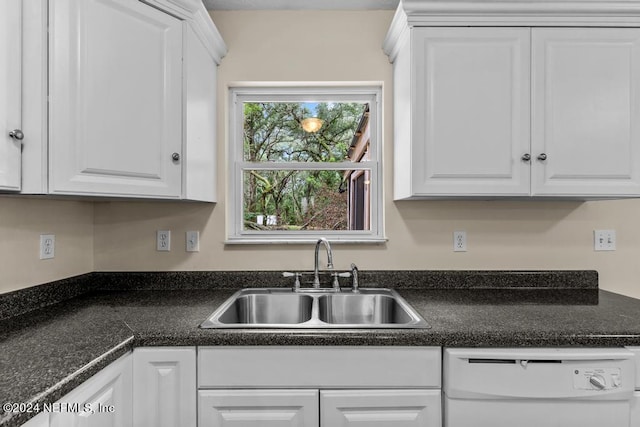 kitchen with dark countertops, white dishwasher, a sink, and white cabinets