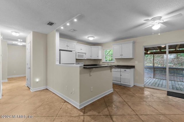 kitchen featuring white appliances, visible vents, white cabinets, dark countertops, and a textured ceiling