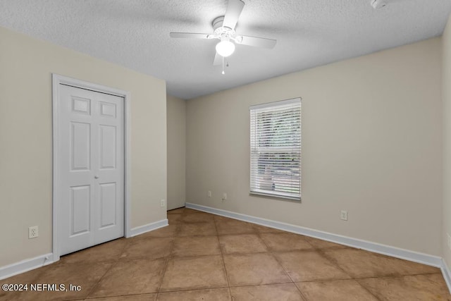 unfurnished bedroom with baseboards, ceiling fan, tile patterned flooring, a textured ceiling, and a closet