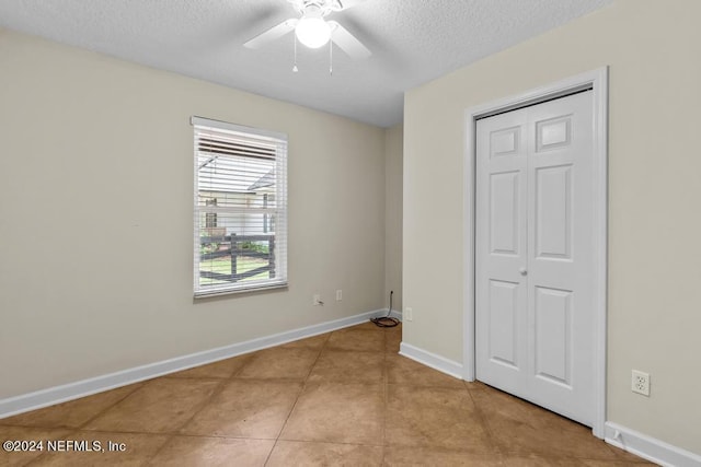 unfurnished bedroom featuring light tile patterned floors, baseboards, a ceiling fan, a textured ceiling, and a closet