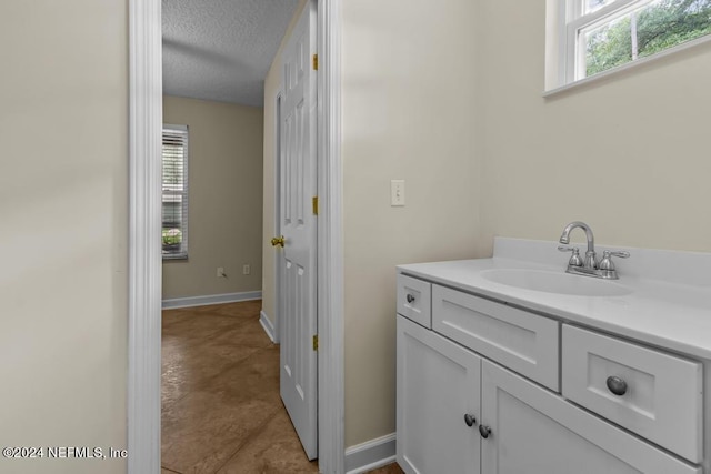 bathroom with a textured ceiling, vanity, and baseboards