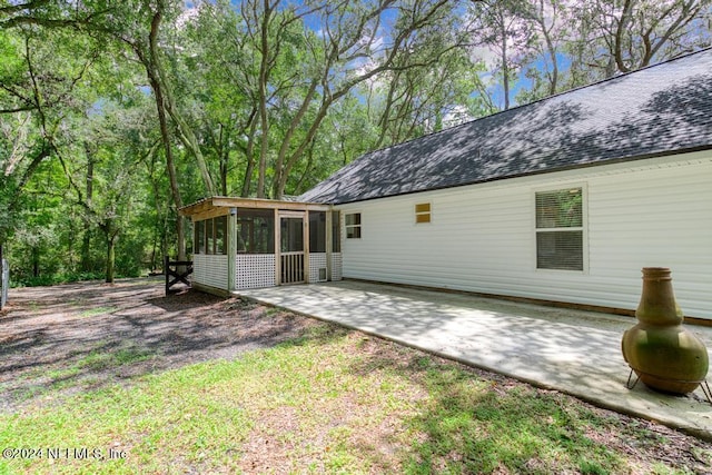 rear view of property with a shingled roof, a sunroom, and a patio