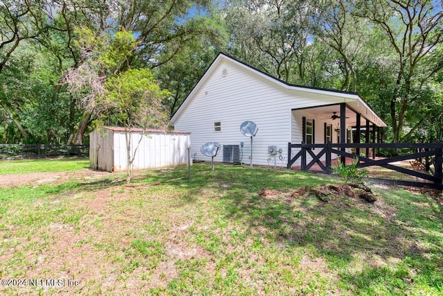 view of home's exterior with central AC, a lawn, an outdoor structure, and fence