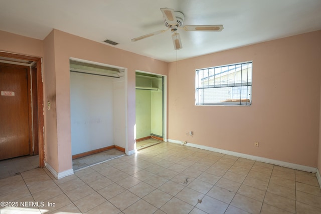 unfurnished bedroom featuring multiple closets, light tile patterned flooring, and ceiling fan