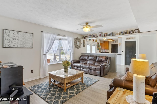 living room featuring ceiling fan, a textured ceiling, and light wood-type flooring