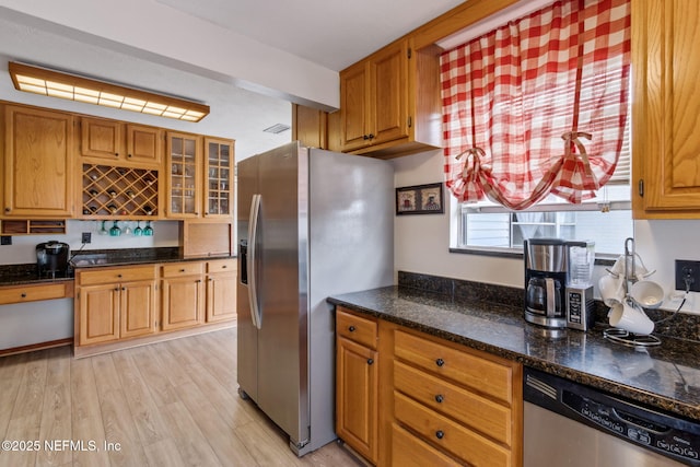 kitchen with appliances with stainless steel finishes, dark stone countertops, and light wood-type flooring