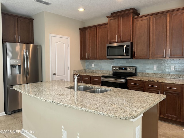 kitchen featuring sink, light tile patterned floors, appliances with stainless steel finishes, a kitchen island with sink, and backsplash