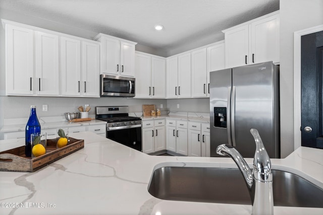 kitchen with white cabinetry, sink, light stone counters, and stainless steel appliances