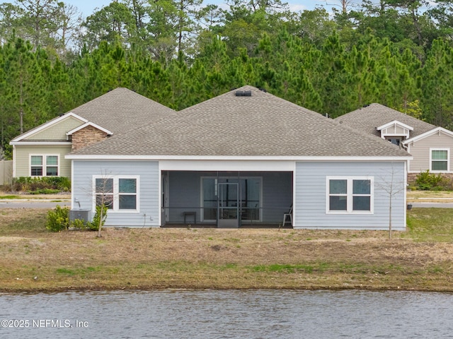 back of house with a water view, a sunroom, and a lawn