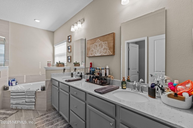 bathroom featuring vanity, tiled bath, and a textured ceiling