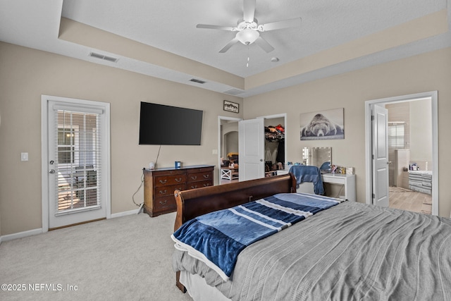 carpeted bedroom with ceiling fan, ensuite bath, a tray ceiling, and a spacious closet