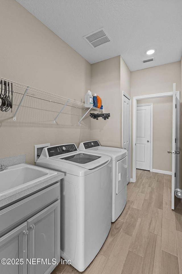 clothes washing area featuring cabinets, sink, washer and dryer, and light hardwood / wood-style flooring