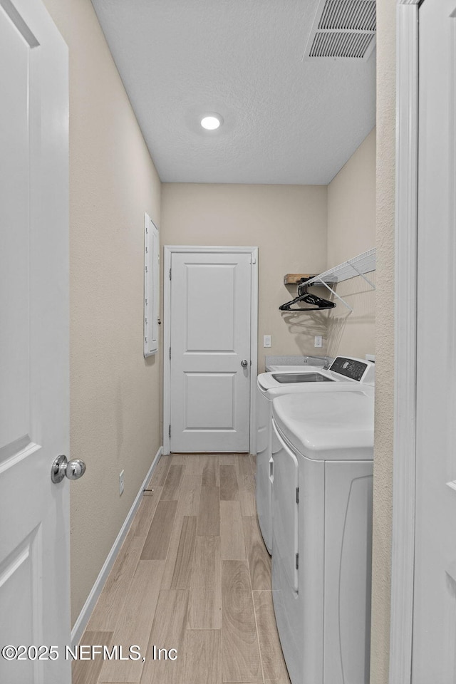 clothes washing area with washer and dryer, a textured ceiling, and light wood-type flooring