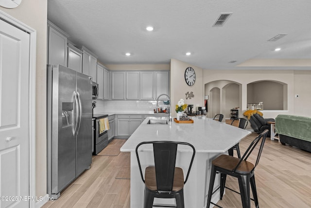 kitchen featuring an island with sink, appliances with stainless steel finishes, a breakfast bar area, and decorative backsplash