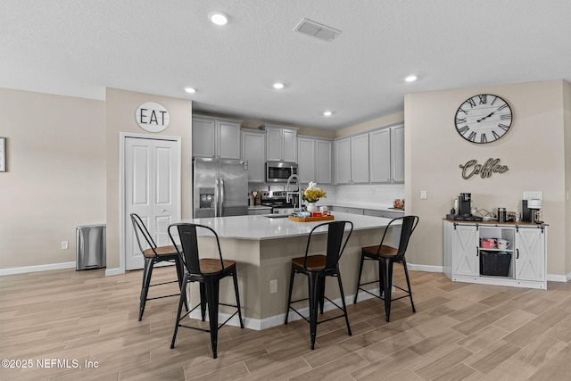 kitchen with an island with sink, appliances with stainless steel finishes, a breakfast bar, and light hardwood / wood-style flooring