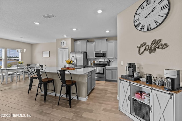 kitchen with pendant lighting, appliances with stainless steel finishes, gray cabinetry, a kitchen island, and a kitchen bar