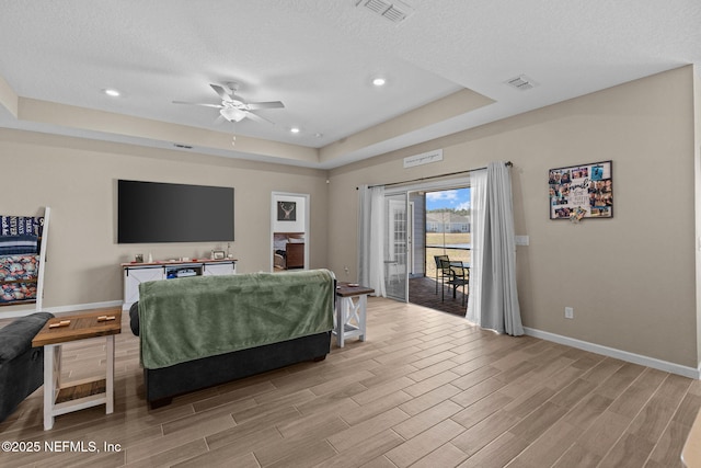 bedroom with ceiling fan, a tray ceiling, light hardwood / wood-style floors, a textured ceiling, and access to outside