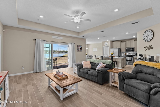 living room featuring a raised ceiling, ceiling fan, a water view, and a textured ceiling