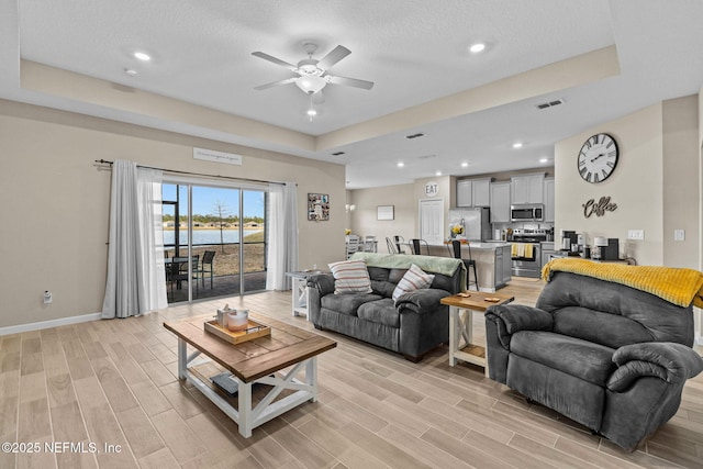 living room with a tray ceiling, a textured ceiling, ceiling fan, and a water view