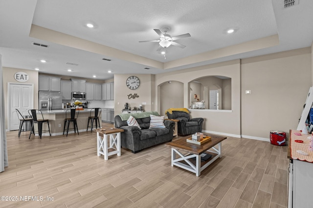 living room featuring a raised ceiling and ceiling fan