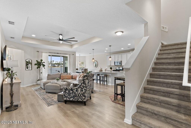 living room with light hardwood / wood-style floors, a tray ceiling, and ceiling fan