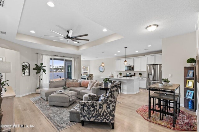 living room with ceiling fan, light wood-type flooring, and a raised ceiling