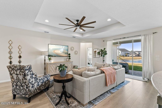 living room featuring ceiling fan, light hardwood / wood-style flooring, a raised ceiling, and a textured ceiling
