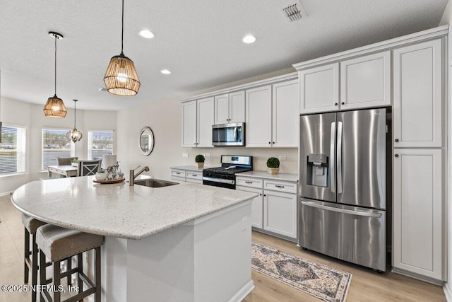 kitchen with a center island with sink, hanging light fixtures, stainless steel appliances, sink, and light stone counters