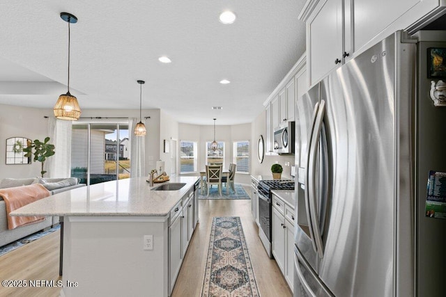 kitchen featuring appliances with stainless steel finishes, white cabinets, hanging light fixtures, light stone countertops, and a kitchen island with sink