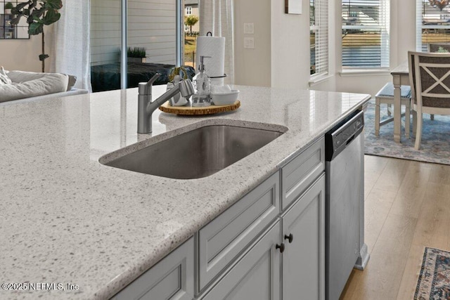kitchen featuring stainless steel dishwasher, light hardwood / wood-style flooring, sink, and light stone counters