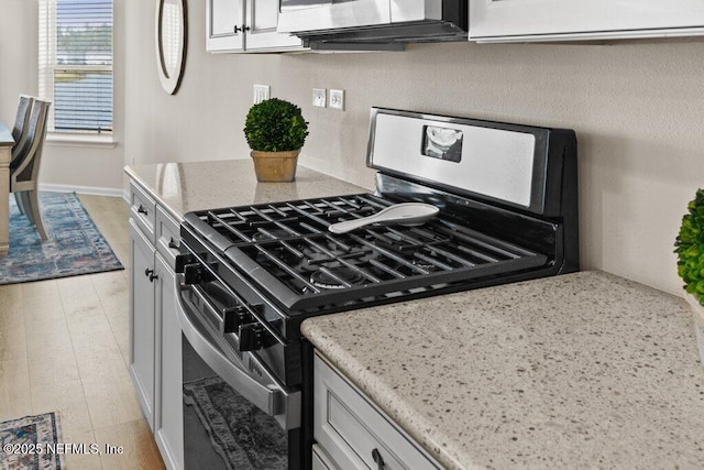 kitchen with stainless steel gas range oven, white cabinetry, light stone countertops, and light hardwood / wood-style floors