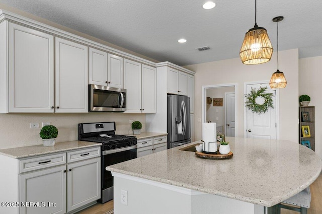 kitchen featuring a center island, decorative light fixtures, light stone counters, appliances with stainless steel finishes, and white cabinets