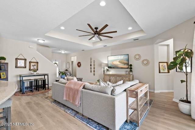 living room featuring a tray ceiling, light hardwood / wood-style flooring, and ceiling fan