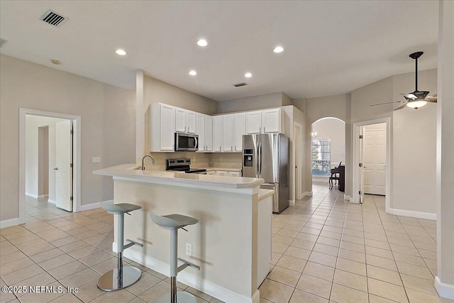 kitchen featuring a kitchen bar, stainless steel appliances, white cabinets, light tile patterned flooring, and kitchen peninsula